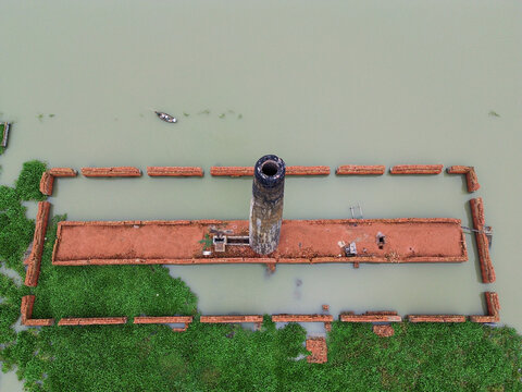 Aerial view of an old brick kiln chimney rising from a flooded structure surrounded by lush green vegetation in the water Dhaka, Dhaka Division, Bangladesh.