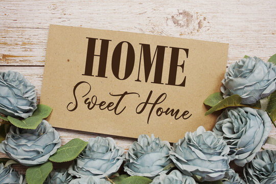 Home Sweet Home text on paper card with rose flowers bouquet on wooden background