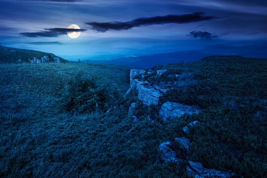 alpine meadow in summer nature at night. full moon over wild grass and grey rocks in carpathian landscape. mountain scenery of perechyn district, ukraine. mysterious fantasy