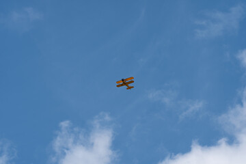A classic yellow propeller biplane cruises through an expansive, vibrant blue sky framed by soft white clouds below. © Sergej