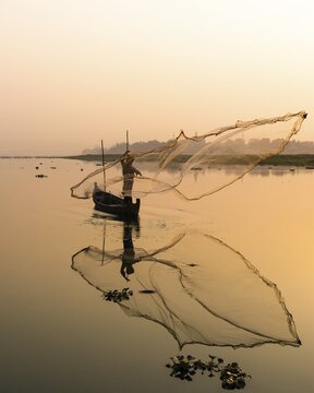 Fisherman with boat on Taung Tha Man Lake casts a fishing net for sunrise, reflection in the water, Thaung Tha Man Lake, Mandalay, Myanmar