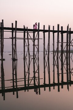 Buddhist monks walk across the U-leg bridge in pink robes as the sun rises, Mandalay, Myanmar