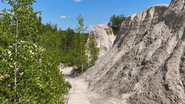 Scenic rocky cliffs and a sandy trail surrounded by lush green forest under a clear blue summer sky, capturing a peaceful natural landscape and outdoor adventure.