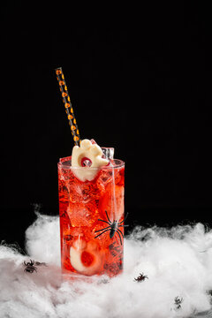 Spooky Halloween Cocktail with Ice Cubes and Ghost Garnish Decorated with Fake Spiders and Cobwebs