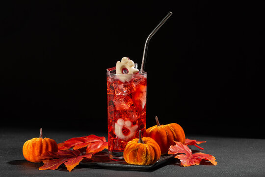 Festive Halloween Red Cocktail Decorated with Ghost Candy and Autumn Pumpkins and Leaves on Dark Background