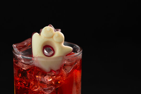 Festive Halloween themed cocktail with ghost shaped marshmallow and red beverage on black background