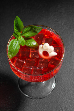 Festive Halloween themed red cocktail with ghost ice cube and fresh basil garnish