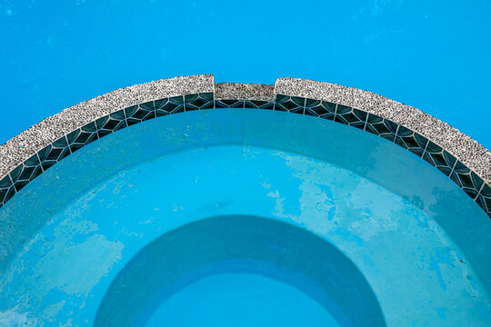 Swimming pool with peeling blue paint and worn plaster on curved steps, pool maintenance and resurfacing concept