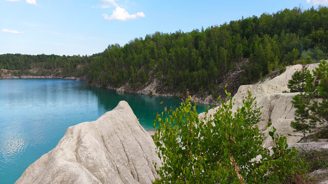 Turquoise lake surrounded by lush green forest and white rocky cliffs under a bright summer sky, creating a peaceful scenic landscape ideal for travel, vacation, and outdoor adventure