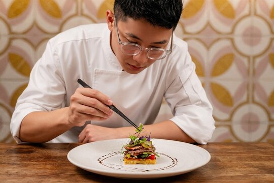 Young Asian chef meticulously plating a gourmet dish in a restaurant  