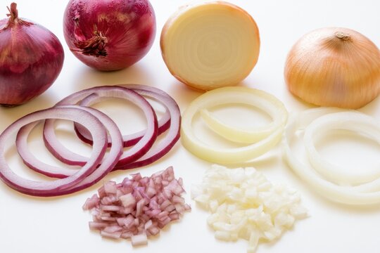 Fresh red and yellow onions arranged with whole bulbs, halved sections, thick rings, thin slices, and diced pieces on a clean white surface for culinary use