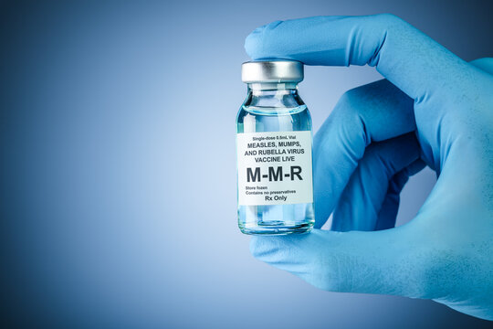 Nurses hand in blue medical gloves holding a vaccine bottle with MMR text. Health care concept of prevention or treatment of measles, mumps, and rubella viruses.