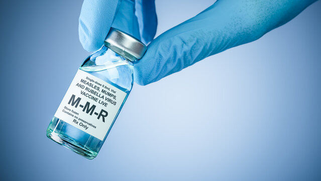 Nurses hand in blue medical gloves holding a vaccine bottle with MMR text. Health care concept of prevention or treatment of measles, mumps, and rubella viruses.