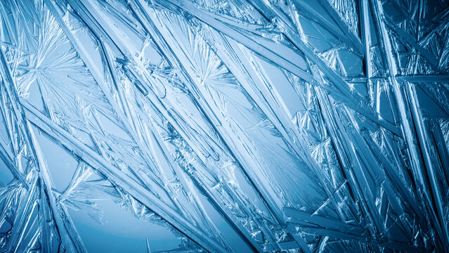 Ice frozen in intricate patterns of delicate crystals with brilliant contrasts of deep blues. Real unique patterned crystal formations. Sparkling window frost or icy cold winter frosting background.