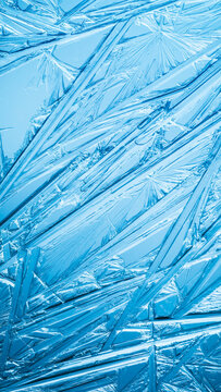 Ice frozen in intricate patterns of delicate crystals with brilliant contrasts of deep blues. Real unique patterned crystal formations. Sparkling window frost or icy cold winter frosting background.