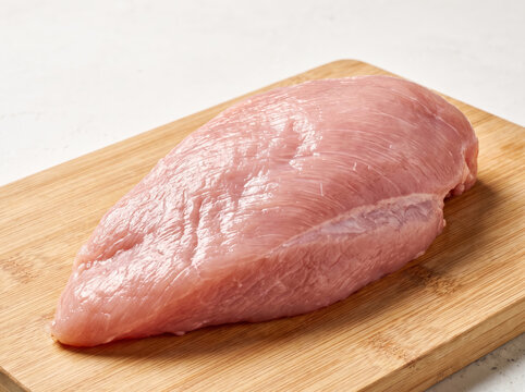 Raw turkey breast fillet placed on a wooden cutting board