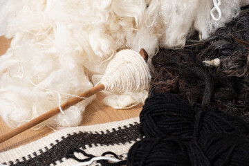 wooden drop spindle with cream yarn rests on raw white and black wool fibers near al sadu textile. al sadu preserves cultural heritage and manual labor. © RollAndSnap