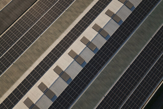 Portugal - 14 August 2026: Aerial view of solar panels installed on industrial factory rooftops, showcasing decentralized renewable energy production with clean geometric patterns.