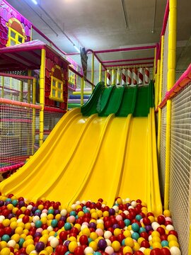 Bright colorful indoor playground slide leading into a ball pit filled with plastic balls.