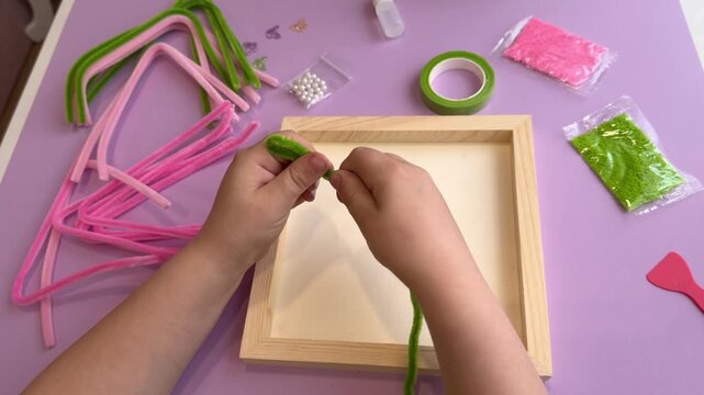 Handmade family activities concept showing a child hands sculpting a decorative plant using plush pipe cleaners and colorful art supplies with extensive copy space left