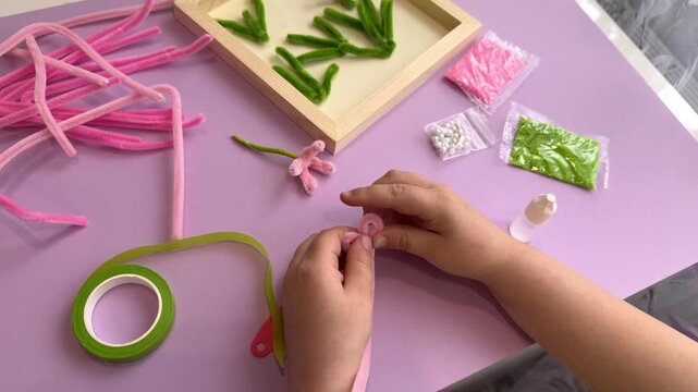 Child hands carefully assembling a soft wire flower centerpiece using premium craft supplies on a pink flat lay table for holiday decoration video template