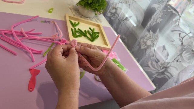 Unrecognizable kid hands folding flexible chenille sticks to create a bright handmade flower for an interactive online tutoring website promotion clip design