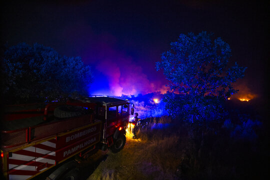 Portugal - 20 August 2026: View of firefighters from Bombeiros Pampilhosa working at night to extinguish a wildfire, with blue emergency lights and flames in the background.