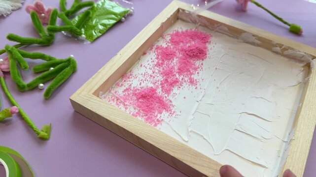 Unrecognizable kid sprinkling decorative glitter powder template on white adhesive canvas during a creative preschool art class or handmade workshop activity on purple desk