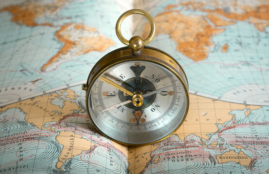 Vintage brass compass on an old geographic map close up. Antique navigation instrument for travel, exploration, geography and discovery concept. 