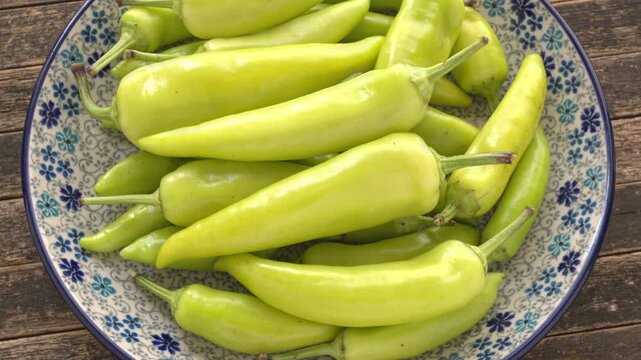 Hungarian Hot Wax peppers pile on a plate. Fresh whole light yellow and green chilies on a ceramic plate. Rustic wooden background, Table spin, backlit window light.