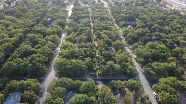 Straight utility corridors bisect heavily forested residential sectors south of Airport Freeway. Shaded asphalt streets, detached homes, thick tree cover highlight neighborhood life, Texas