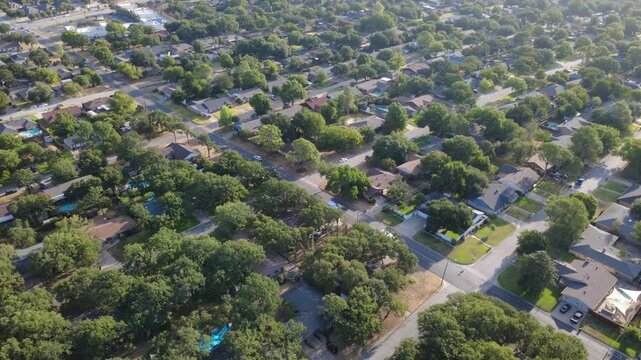 Broad asphalt intersections cross wooded neighborhood streets south of Airport Freeway. Shaded driveways, single story ranch houses, lush oak canopies illustrate peaceful living, Hurst, Texas