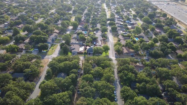 Orderly residential blocks stretch northward toward fast moving traffic lanes on Airport Freeway. Continuous shade trees, utility lines, single story homes represent DFW sprawl, Hurst, Texas