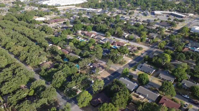 Diagonal roadway junctions link quiet neighborhood properties near Airport Freeway. Mature oak trees, private driveways, single family dwellings demonstrate residential growth, Hurst, Texas
