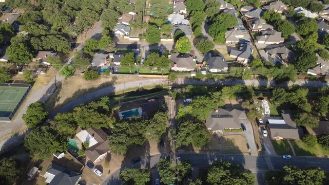 Riprap stone drainage embankments separate private backyard pools from Little Bear Creek parkland. Enclosed courts, parked trailers, mature hardwood trees reveal residential pockets, Hurst, Texas
