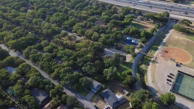 Municipal sports parks adjoin peaceful residential enclaves along Little Bear Creek. Dirt ballfields, playground canopies, shaded neighborhood streets illustrate civic spaces, Hurst, Texas