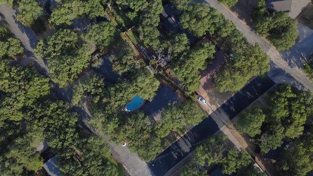 Freshly resurfaced asphalt lanes curve past wooded residential tracts west of Precinct Line Road. Kidney shaped pools, shaded rooflines, parked cars display suburban tranquility, Hurst, Texas