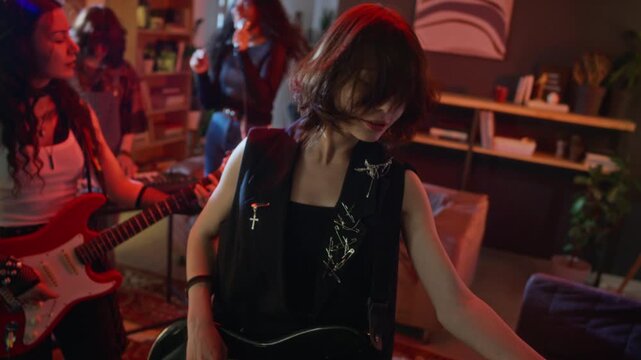 Teenage girl playing bass guitar and headbanging during music rehearsal with diverse band members at home. Footage is ideal for youth culture advertisements or music school promos