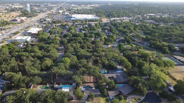 Curving suburban driveways surround secluded backyard swimming pools adjacent to Hurst Community Park. Paved lanes, private fences, dense tree cover represent classic suburban life, Texas