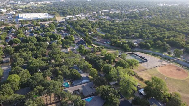 Public athletic fields adjoin peaceful single family neighborhood tracts bordering Little Bear Creek. Dirt diamonds, fenced courts, mature greenery illustrate local civic spaces, Hurst, Texas