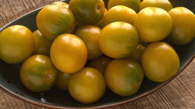 Tomatoes of Green Grape Cherry variety rotating smoothly on an oval blue platter, vertical video.