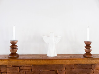 Fototapeta premium White Angel Figurine and Candles on Wooden Shelf Above Stone Fireplace