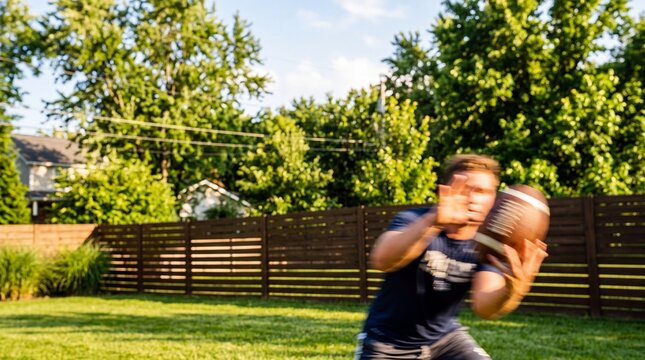 Man Catching American Football in Backyard Lawn