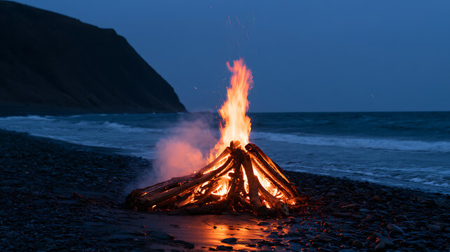 Bright campfire burn on dark ocean beach with high cliff in twilight. Cozy night landscape scene by sea water and pebble shore