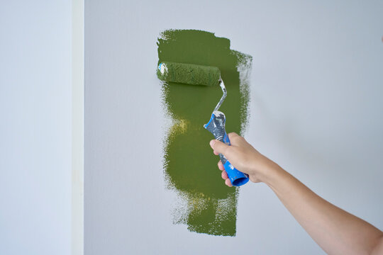 Hand applies green paint to white wall with a small roller to test the color