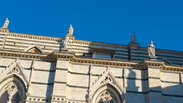 Siena cathedral facade and bell tower. Majestic siena cathedral facade showcasing intricate details, statues, and striped marble patterns, along with its towering bell tower against a vibrant blue sky