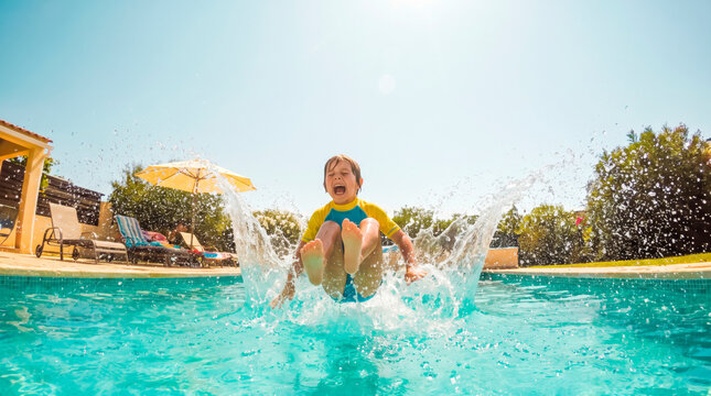 Joyful Splash: A young boy exuberantly jumps into a sparkling blue swimming pool, sending water splashing high into the air under a clear sunny sky.