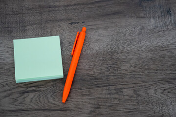 Blank green sticky note pad and orange pen on dark wooden desk background © Mihail