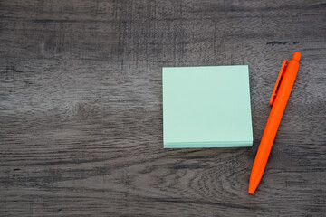 Blank green sticky note pad and orange pen on dark wooden desk background © Mihail