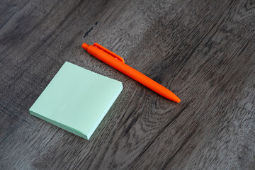 Blank green sticky note pad and orange pen on dark wooden desk background © Mihail
